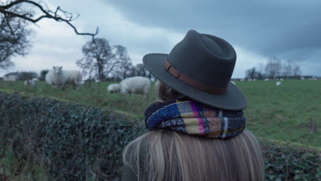 Woman-walking-past-field-of-sheep
