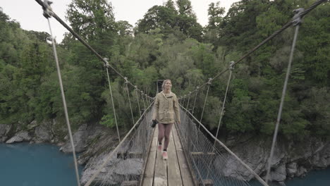 Attractive-European-female-tourist-walking-on-suspension-bridge-at-Hokitika-Gorge