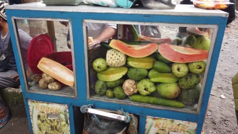 Rujak-Street-Food,-Spicy-Fruit-Salad,-Vendor-in-Indonesia-Bali-Southeast-Asia-prepares-a-Traditional-Popular-Dish-with-Papaya,-Carambola,-Mango,-Cucumber-and-Sauce-in-Saba-Beach,-Gianyar