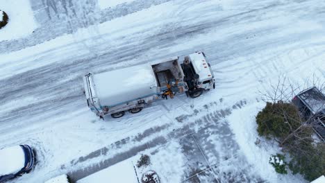 Overhead-aerial-view-of-a-garbage-truck-picking-up-trash-in-icy-conditions