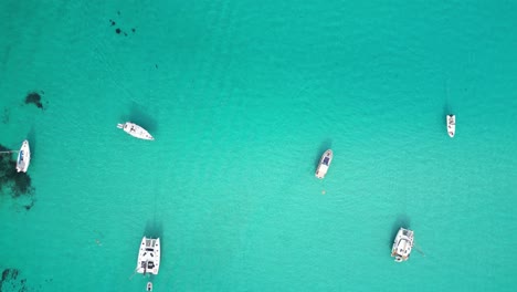 Boats-floating-at-turquoise-blue-sea-at-La-Pelosa,-Sardinia,-Italy---Aerial-4k-Birdseye
