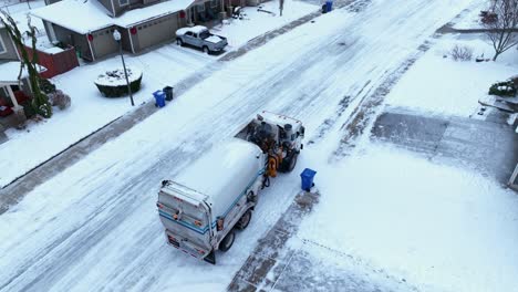 Aerial-shot-of-a-truck-picking-up-trash-in-a-suburban-neighborhood-covered-in-snow