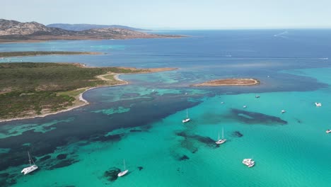 Boats-in-turquoise-blue-sea-at-La-Pelosa-near-Asinara-National-Park,-Sardinia,-Italy---Aerial-4k-Backwards