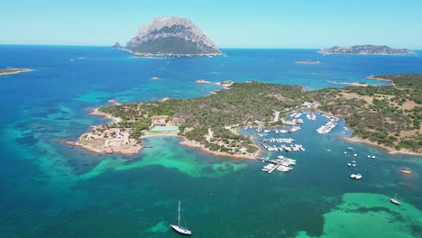 Porto-San-Paolo-and-Tavolara-Island-surrounded-by-boats-and-turquoise-blue-sea-in-Sardinia,-Italy---Aerial-4k