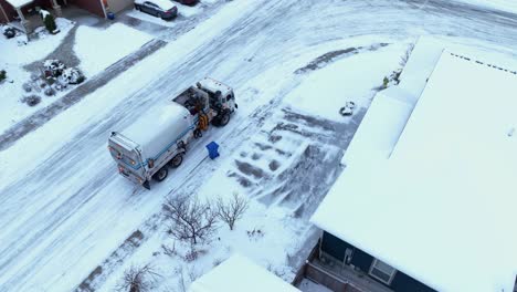 Orbiting-aerial-view-of-a-public-utility-truck-picking-up-trash-on-a-snowy-day