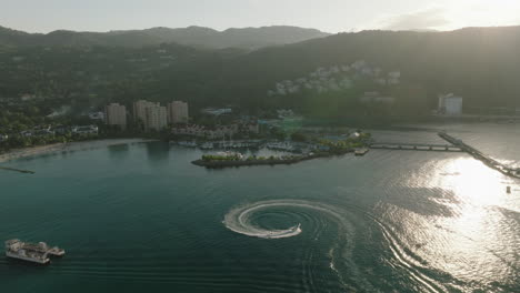 Barco-Haciendo-Círculos-En-Una-Bahía-Jamaicana-Con-Hermosas-Aguas-Azules-Y-Un-Entorno-Montañoso