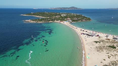 Windsurfer-surfs-along-white-sandy-beach-towards-peninsula-island-at-Porto-Pollo,-Sardinia---4k-Aerial