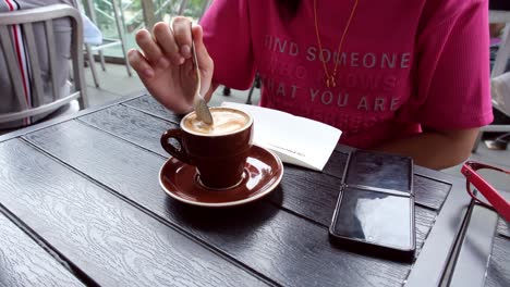 Eine-Person,-Die-Eine-Tasse-Kaffee-Mit-Einem-Rosa-Lockeren-Hemd-Und-Einem-Telefon-Auf-Dem-Tisch-Trinkt