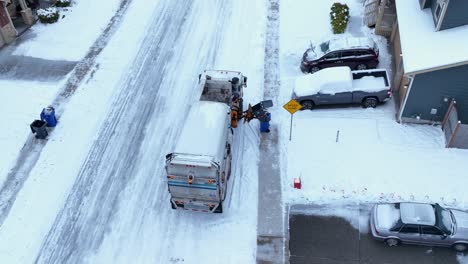 Aerial-shot-of-a-garbage-truck-picking-up-trash-despite-the-icy-streets