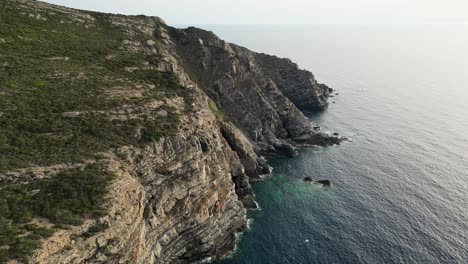 Steef-cliffs-and-rocky-coastline-during-twilight-at-La-Pelosa,-Sardinia---Aerial-4k