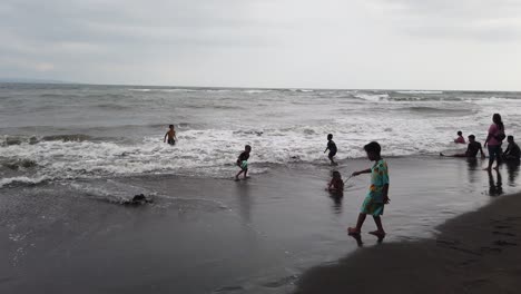 Kinder-Spielen-Mit-Fußball-Am-Strand,-Haben-Spaß-Am-Meerwasser-Von-Bali,-Indonesien,-Saba,-Gianyar,-Schwarzem-Sand,-Kinderfreundschaft,-Südostasien