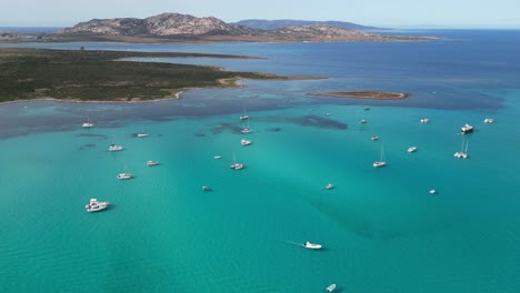 Boats-floating-at-turquoise-blue-sea-near-Isola-Piana-Island,-La-Pelosa,-Sardinia,-Italy---Aerial-4k-Circling