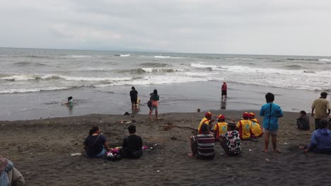 People-and-Families-Gather-at-Local-Black-Sand-Beach-in-Bali-Indonesia,-Saba,-Gianyar,-Typical-Sunday-Activity,-Strong-Waves,-Sea-and-Ocean-in-Southeast-Asia