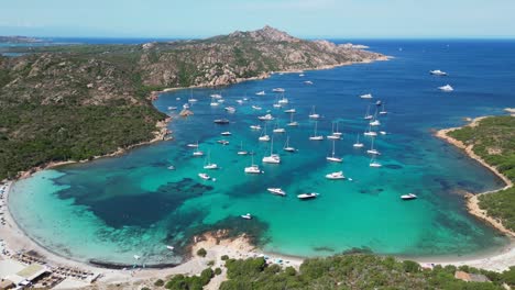 Boats-and-yachts-floating-in-turquoise-blue-cove-at-La-Maddalena-Island,-Sardinia---Scenic-Aerial-4k