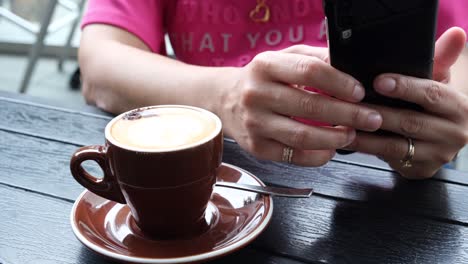 A-person-hand-holding-a-phone-while-having-cup-of-coffee