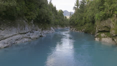 Blue-mountain-meltwater-flowing-through-rock-Hokitika-Gorge,-low-aerial