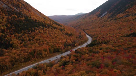 Aerial-of-road-between-two-mountains-surrounded-by-fall-foliage