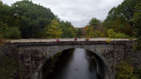 Young-man-sits-on-a-gravel-path-on-a-bridge-over-a-river-in-the-fall