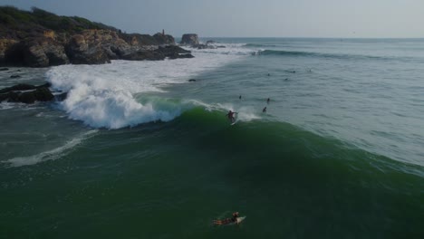 Aerial-view-tracking-surfer-riding-waves-along-Punta-Zicatela-Oaxaca-sunny-blue-sea-coastline,-Mexico