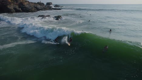 Aerial-view-reversing-across-surfers-riding-powerful-wave-on-Punta-Zicatela-sunlit-Pacific-ocean-Oaxaca-seascape