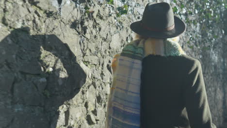 Schatten-Der-Gehenden-Frau-Auf-Steinmauer,-Die-Ihren-Hut-Justiert