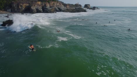 Aerial-view-panning-across-surfers-riding-waves-on-Punta-Zicatela-sunlit-Oaxaca-Pacific-ocean-seascape