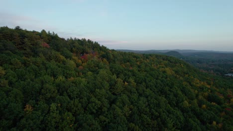 Aerial-of-trees-in-a-forest-on-the-top-of-a-mountain-surrounded-by-fall-foliage-and-greenery