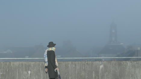 Woman-walks-across-the-rooftop-looking-at-city-watch-tower-in-misty-sunny-day