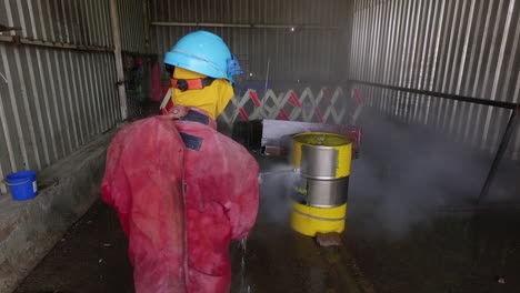 Man-in-work-overall-using-high-pressure-cleaning-equipment-to-blast-paint-of-an-oil-barrel