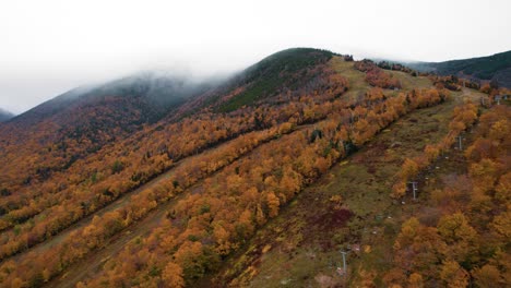 Aerial-of-a-mountain-with-fall-foliage-surrounded-by-clouds