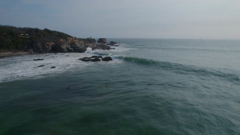 Aerial-view-surfers-riding-waves-in-Punta-Zicatela-Oaxaca-blue-sea,-Mexico-waterfront