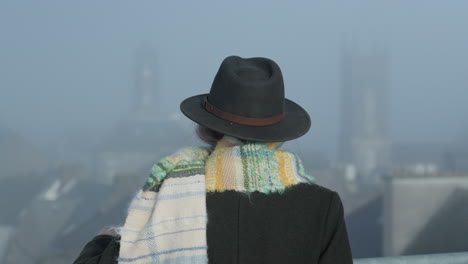 Woman-in-hat-looking-at-city-church-towers-in-misty-morning