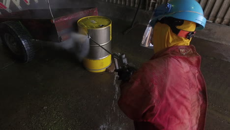 Man-using-a-high-pressure-washing-equipment-to-strip-paint-off-an-oil-drum