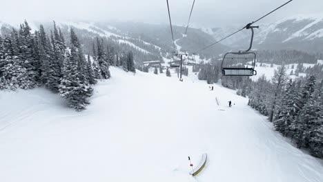 POV-Empty-chairlift-over-ski-slope-with-big-pine-trees-at-ski-resort-during-winter