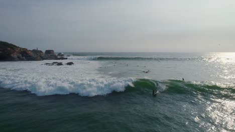 Aerial-backward-dolly-shot-of-surfers-waiting-and-catching-waves