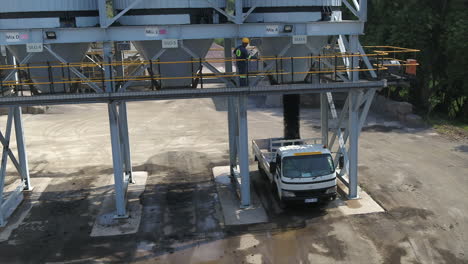 Aerial-drone-shot-of-a-truck-being-loaded-with-asphalt-at-an-asphalt-plant