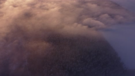 Flying-over-fog-mist-clouds-and-frost-covered-seasonal-forests-in-sunrise-light