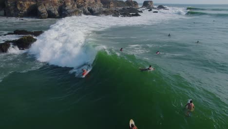 Aerial-panning-view-of-surfers-riding-waves-on-Punta-Zicatela-sunlit-Oaxaca,-Mexico-coastline