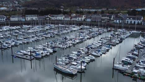 Scenic-luxurious-waterfront-harbour-apartment-village-yachts-and-sailboats-under-mountain-coastline-aerial-view-zoom-in