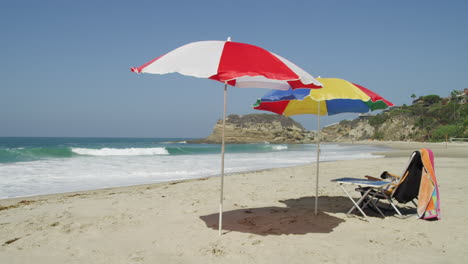 Folding-Chair-And-Colorful-Umbrellas-At-Empty-Beach-On-A-Sunny-Summer-Day