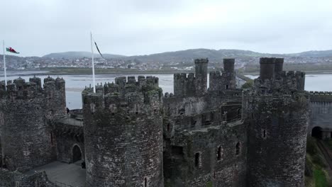 Flags-on-historic-Conwy-castle-aerial-view-of-Landmark-town-ruin-stone-wall-battlements-tourist-attraction-orbit-right-shot