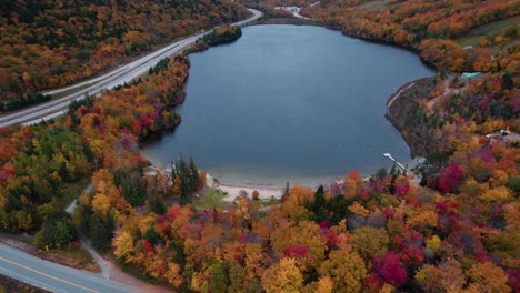 Aerial-of-blue-lake-in-the-mountains-surrounded-by-fall-foliage