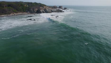 Aerial-view-above-surfers-riding-waves-in-Punta-Zicatela-sunny-pacific-ocean-Oaxaca-coastline