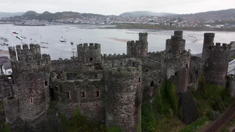 Historic-Conwy-castle-aerial-view-of-Landmark-town-ruin-stone-wall-battlements-tourist-attraction-pull-back-right-orbit