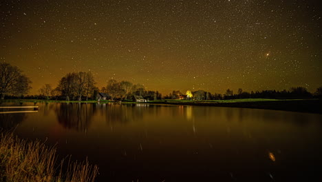 Time-lapse-shot-of-rotating-stars-on-yellow-black-colored-sky-at-night-and-reflection-on-water-surface-in-lake