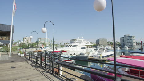 POV-Of-A-Person-Walking-At-Boardwalk-Along-Newport-Beach-Harbor-With-Yachts-And-Boats-On-A-Sunny-Summer-Day