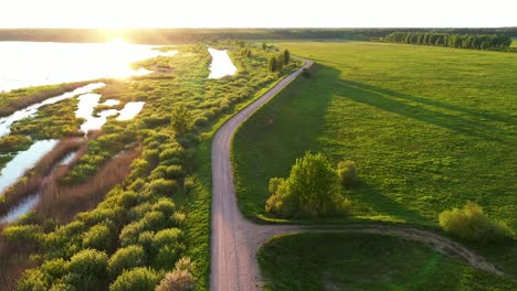 Long-pathway-aerial-view-descending-across-green-marsh-wetland-during-golden-sunrise