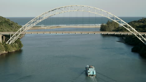 Luftdrohne-Schoss-Ein-Freizeitboot-Auf-Einem-Fluss-Mit-Einer-Hängebrücke-Im-Hintergrund