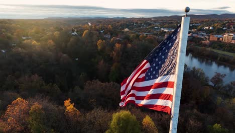 Cinematic-aerial-of-American-flag-waving-in-breeze-during-autumn-golden-hour-sunrise-light