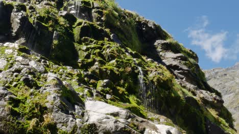 Several-small-waterfalls-flowing-down-rocky-mountains-covered-with-moss-during-sunny-day-at-Gertrude-Saddle-Hike-in-New-Zealand